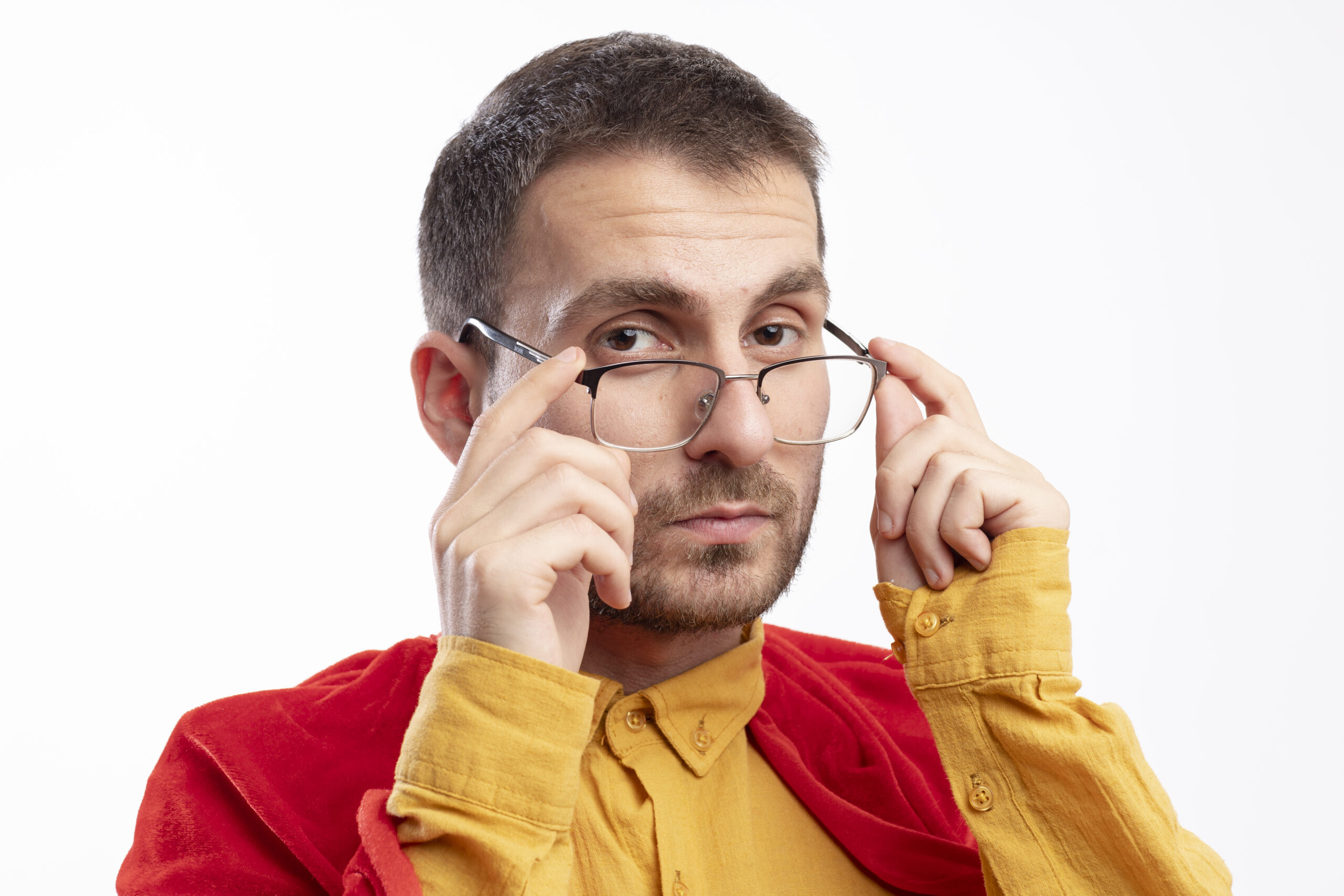 confident caucasian superhero man with red cloak holds optical glasses and looks at camera isolated on white background with copy space