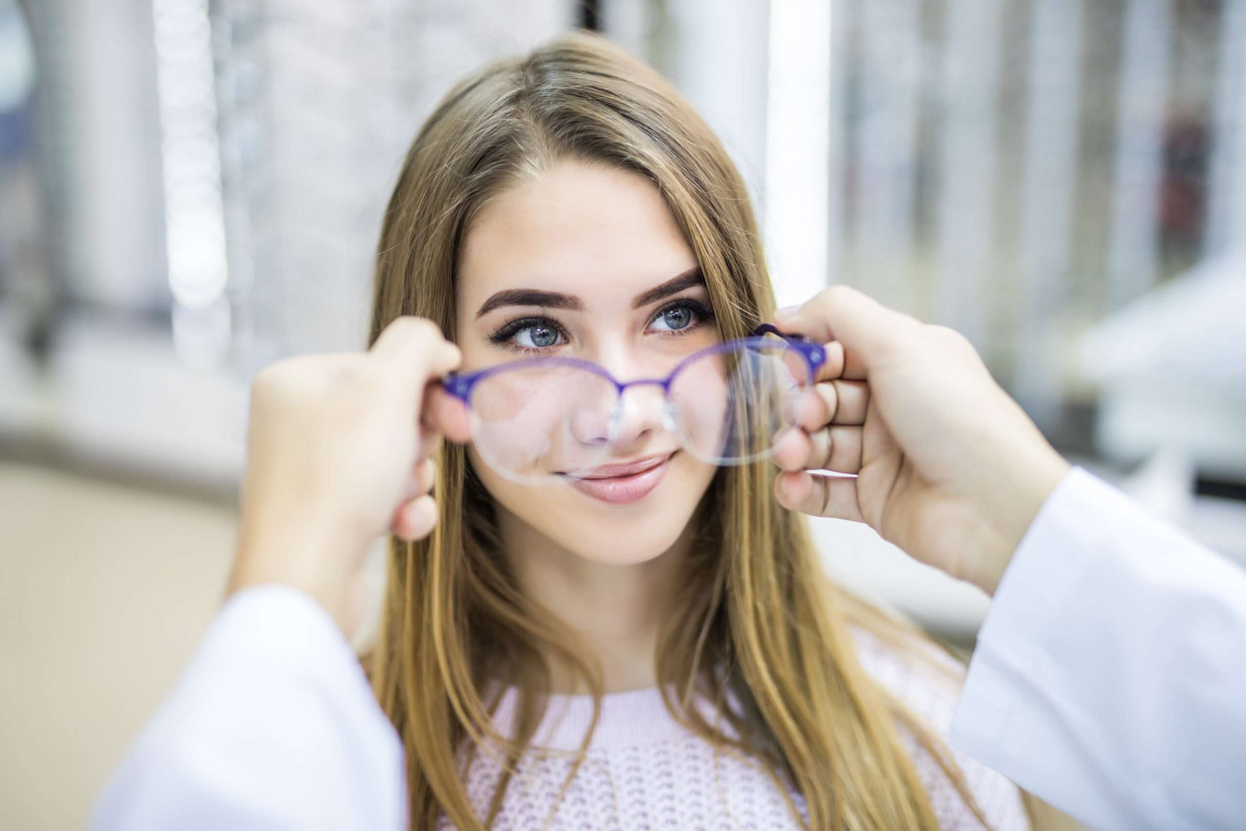 Optician helping a young woman try on eyeglasses during an eye care consultation.